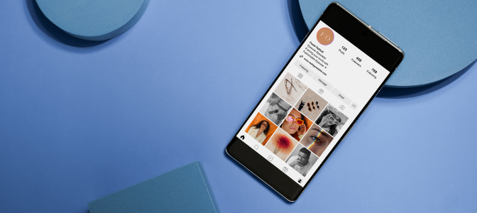 Perfil de Instagram exibido em um smartphone sobre uma superfície azul, destacando uma estratégia de marketing nas redes sociais com fotos e informações organizadas.