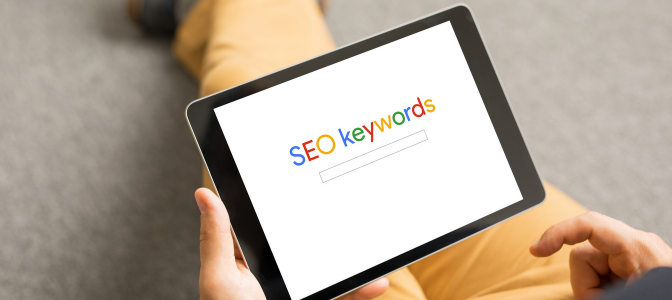 Pessoa segurando um tablet com a tela exibindo o texto “SEO keywords”, representando o conceito de otimização de sites em Curitiba.