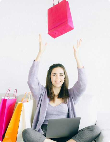 Mulher comemorando vendas online, sentada com notebook e sacolas de compras, representando sucesso em loja virtual e e-commerce profissional.